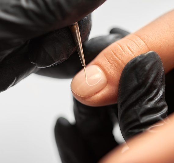 Professional manicurist hands painting elegant abstract patterns on woman nails using applicator. Process of making fashionable manicure in beauty salon. Close-up of professional master manicurist hands painting patterns on client woman nails using applicator on light blurred background.